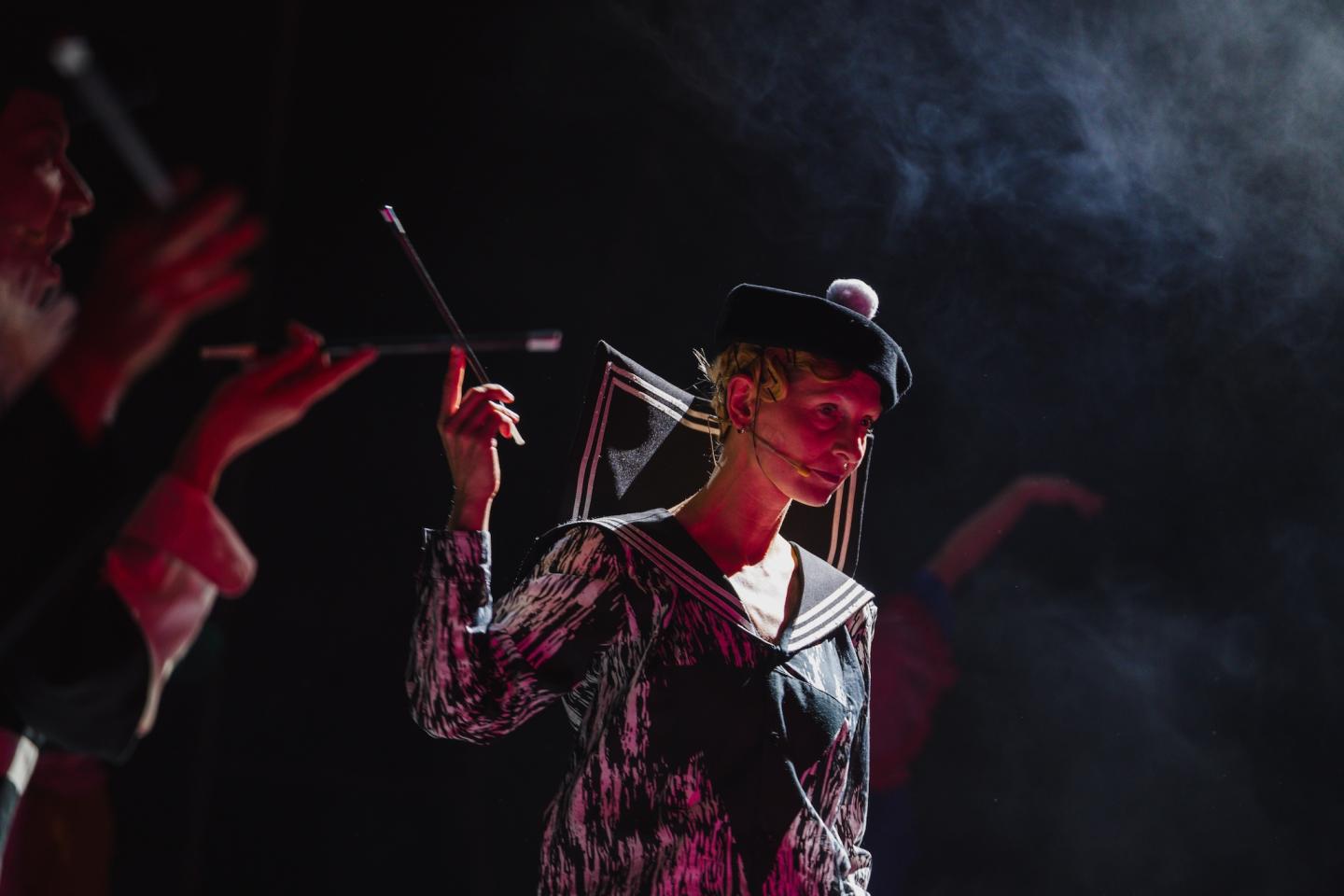 Kobieta ubrana w czarno-biały strój stoi w półmroku. Nad nią unosi się dym. Unosi lewą rękę, w której trzyma cygaretkę. Na głowie ma ubrany czarny beret z białym pomponem.